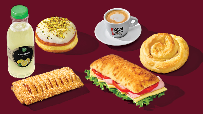 Boca limunade, krafna s bijelom glazurom i mljevenim pistacijama, lisnato pecivo s punjenjem posuto sezamom, sendvič u ciabatti sa sirom, šunkom, rajčicom i zelenom salatom, šalica espressa te lisnato pecivo u obliku puža na tamnocrvenoj podlozi.