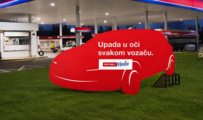 Crvena reklamna instalacija u obliku automobila postavljena na travnatoj površini uz Petrolovo prodajno mjesto, s istaknutom porukom ‘Upada u oči svakom vozaču’.